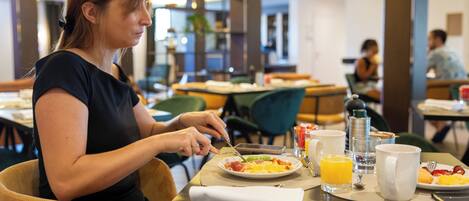 Una mujer desayunando en el restaurante de un hotel, con una mesa dispuesta que incluye huevos, tostadas y jugo de naranja.