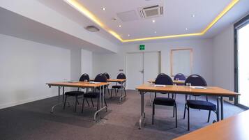 A conference room with tables and chairs, a door with an emergency exit sign, and a window on the right.