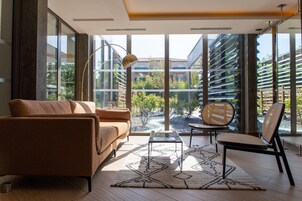 Un salón moderno con un sofá, una silla, una mesa de centro y un ventanal con vistas a un edificio y zonas verdes.