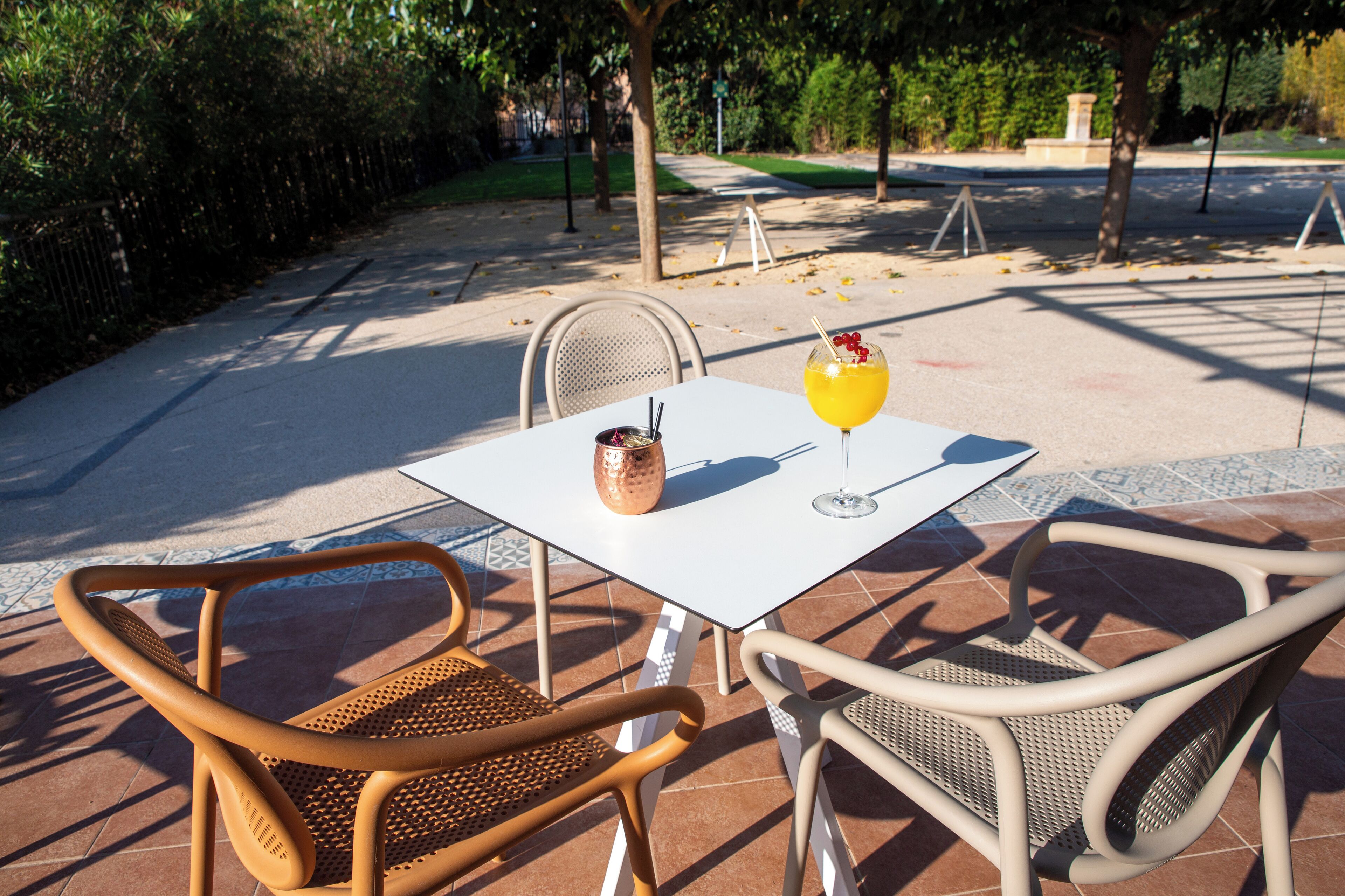Un patio al aire libre con una mesa y sillas, una bebida sobre la mesa y vistas a un parque al fondo.