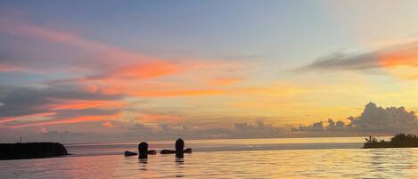A calm body of water reflecting a sunset sky with a crescent moon visible.