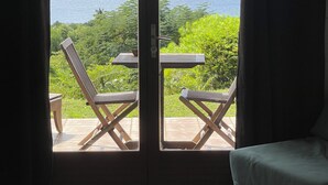 Una stanza con un letto, un tavolo e due sedie rivolte a un balcone con vista sull'oceano e sul verde.
