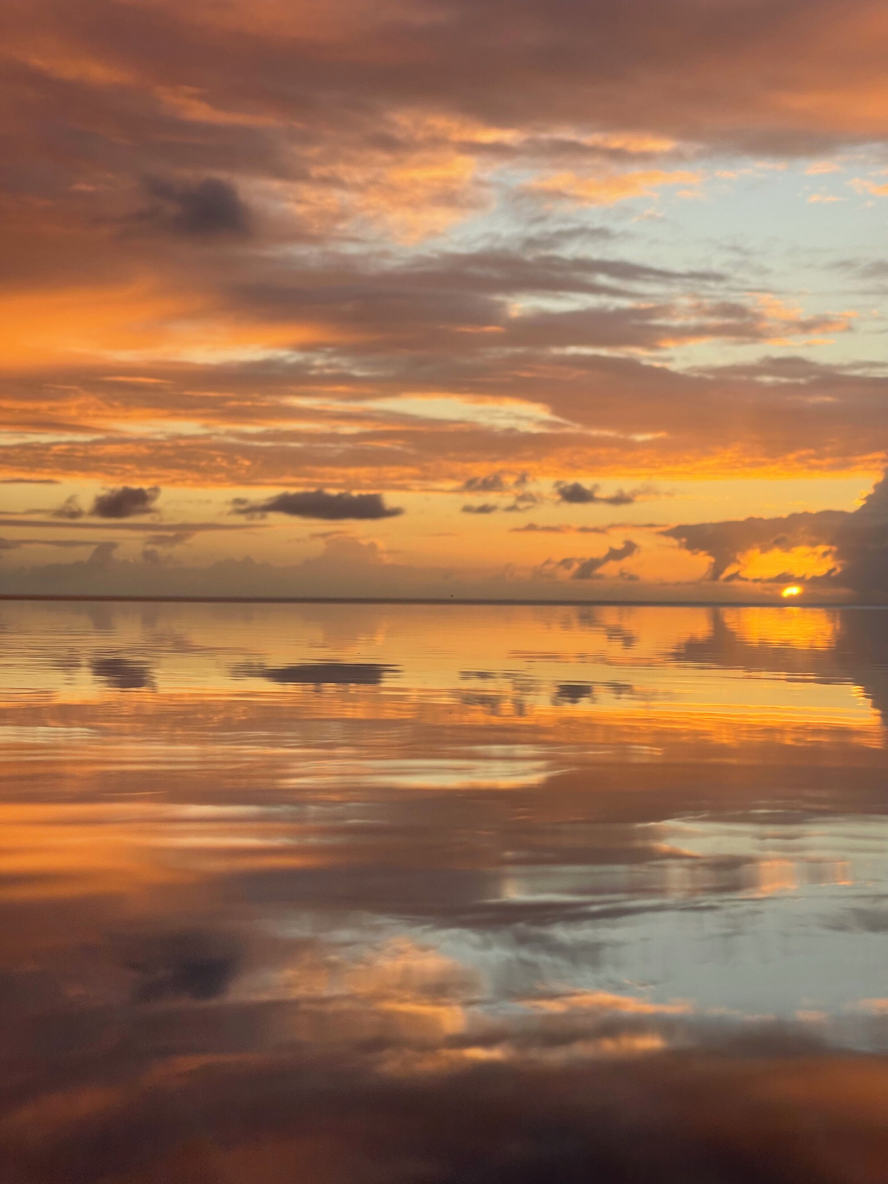Un coucher de soleil sur une étendue d’eau calme, dont la surface reflète le ciel.