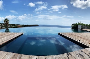 Una piscina infinita de color azul intenso con bordes de madera, rodeada de exuberante vegetación y vista al océano.