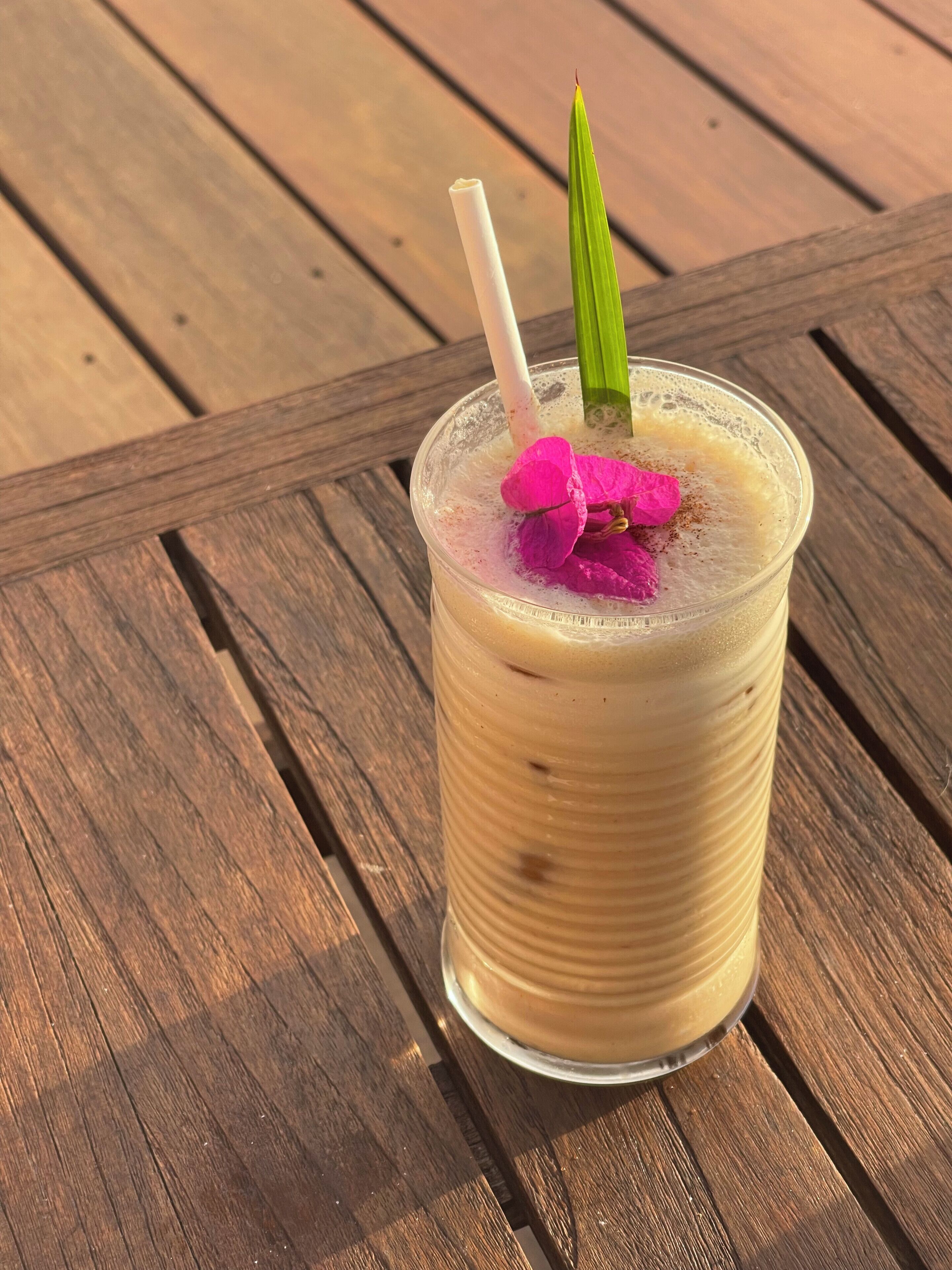 Un verre transparent contenant une boisson, avec une paille et une feuille verte en guise de décoration, posé sur une table en bois.