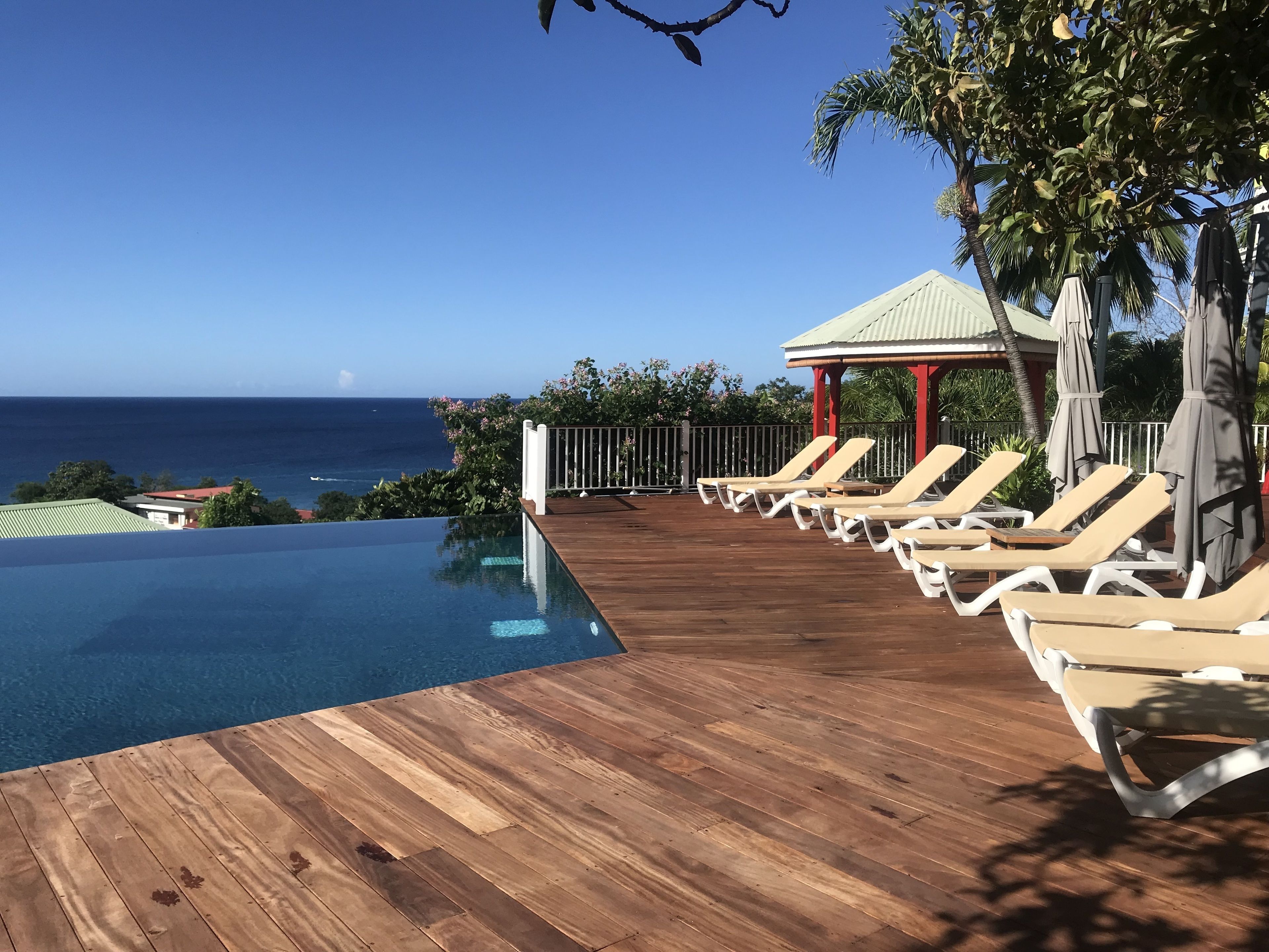 An infinity pool with wooden deck, lounge chairs, and a gazebo overlooking the ocean.