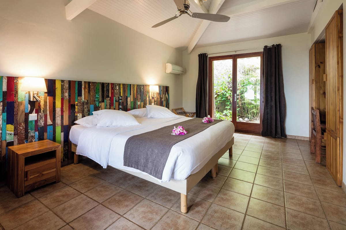 Un dormitorio espacioso con una cama grande, un ventilador de techo y vistas a zonas verdes por la ventana.