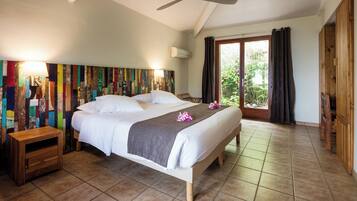 A spacious bedroom with a large bed, a ceiling fan, and a view of greenery through the window.