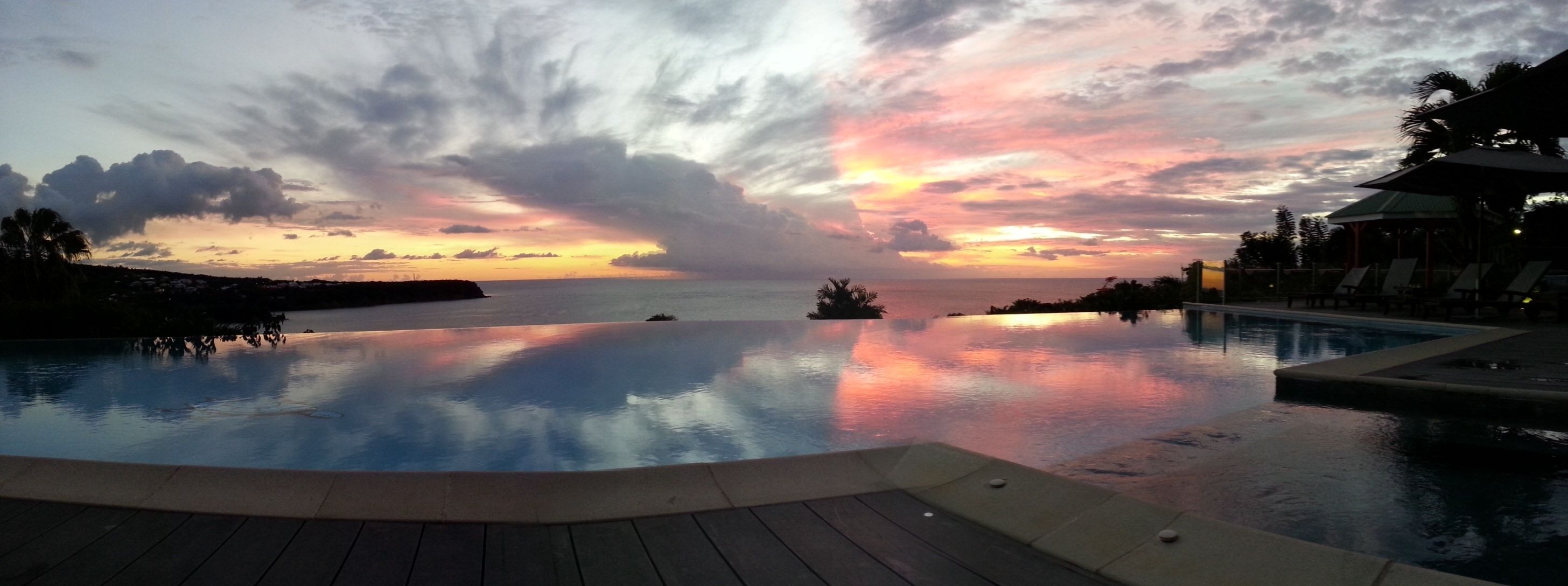 Piscina con vista al atardecer, sillas de descanso y una palmera.