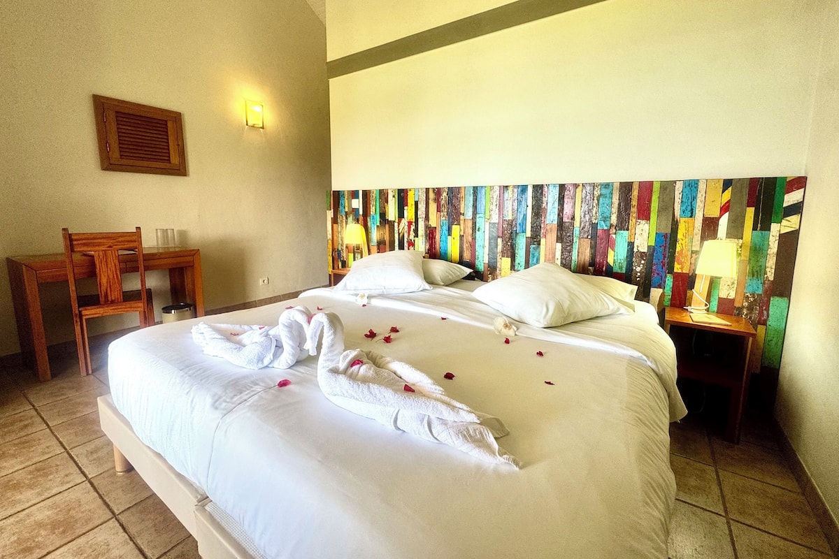 Habitación de hotel con cama, una silla, una mesita de noche, una lámpara y un cuadro de pared colorido.