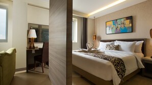 Una habitación de hotel con cama, escritorio, silla y un cuadro en la pared.