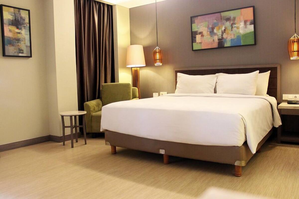 A hotel room with a large bed, a green armchair, a small table, and two wall-mounted lamps.