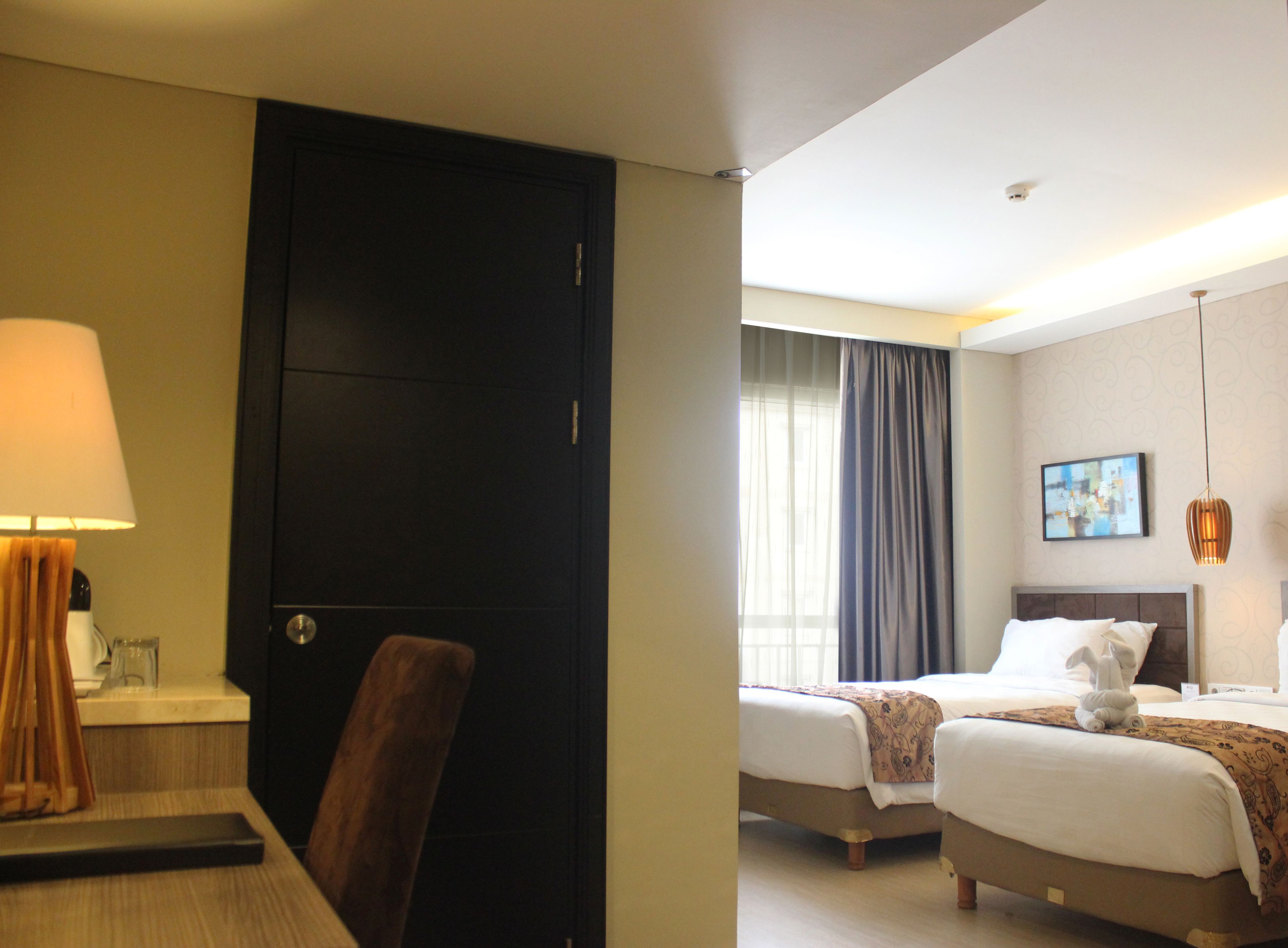 A hotel room with a desk, chair, two beds, a lamp, and a window with curtains.