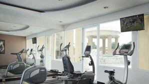 Un gimnasio con cintas de correr, elípticas y una pantalla de televisión que muestra un evento deportivo.