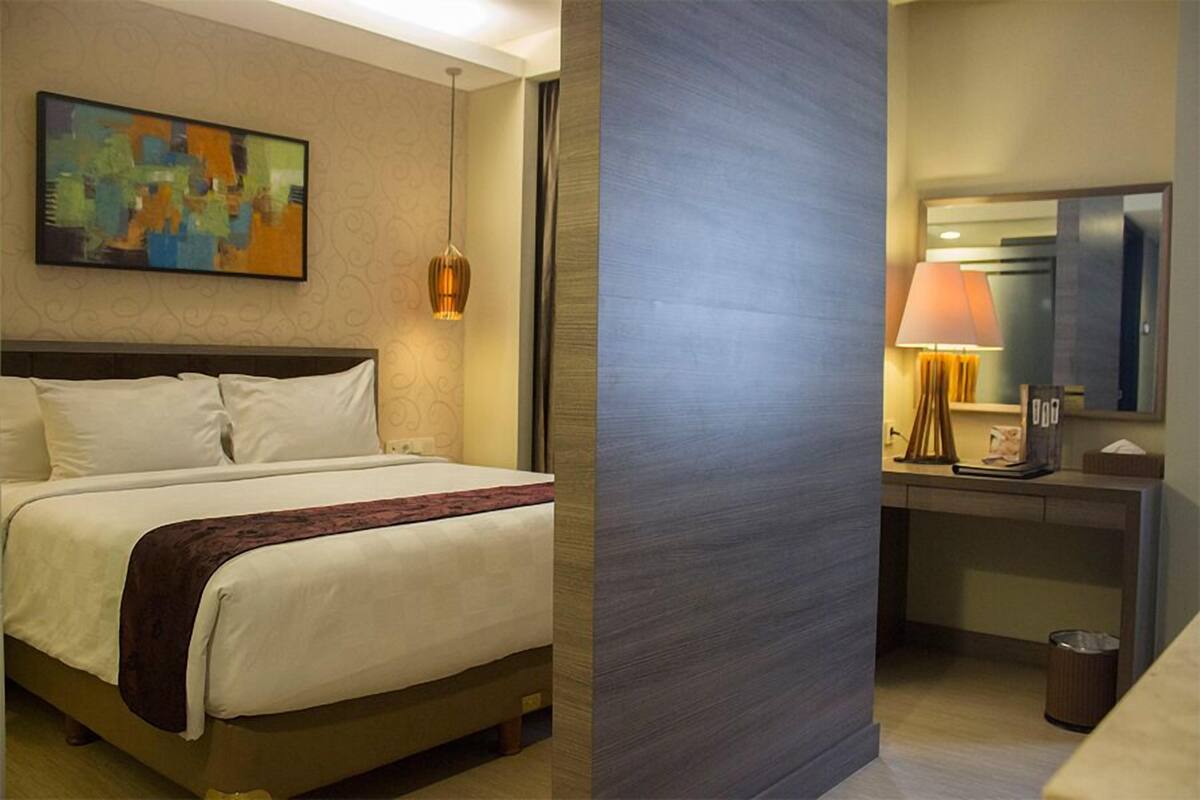 A hotel room with a bed, a desk, a lamp, and a painting on the wall.