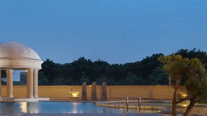 Un quiosco con columnas y cúpula, rodeado por una piscina y árboles.
