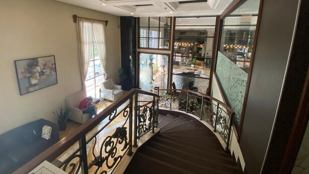 Una escalera con barandillas decorativas que lleva a un balcón con vistas a un restaurante y mesas al aire libre.