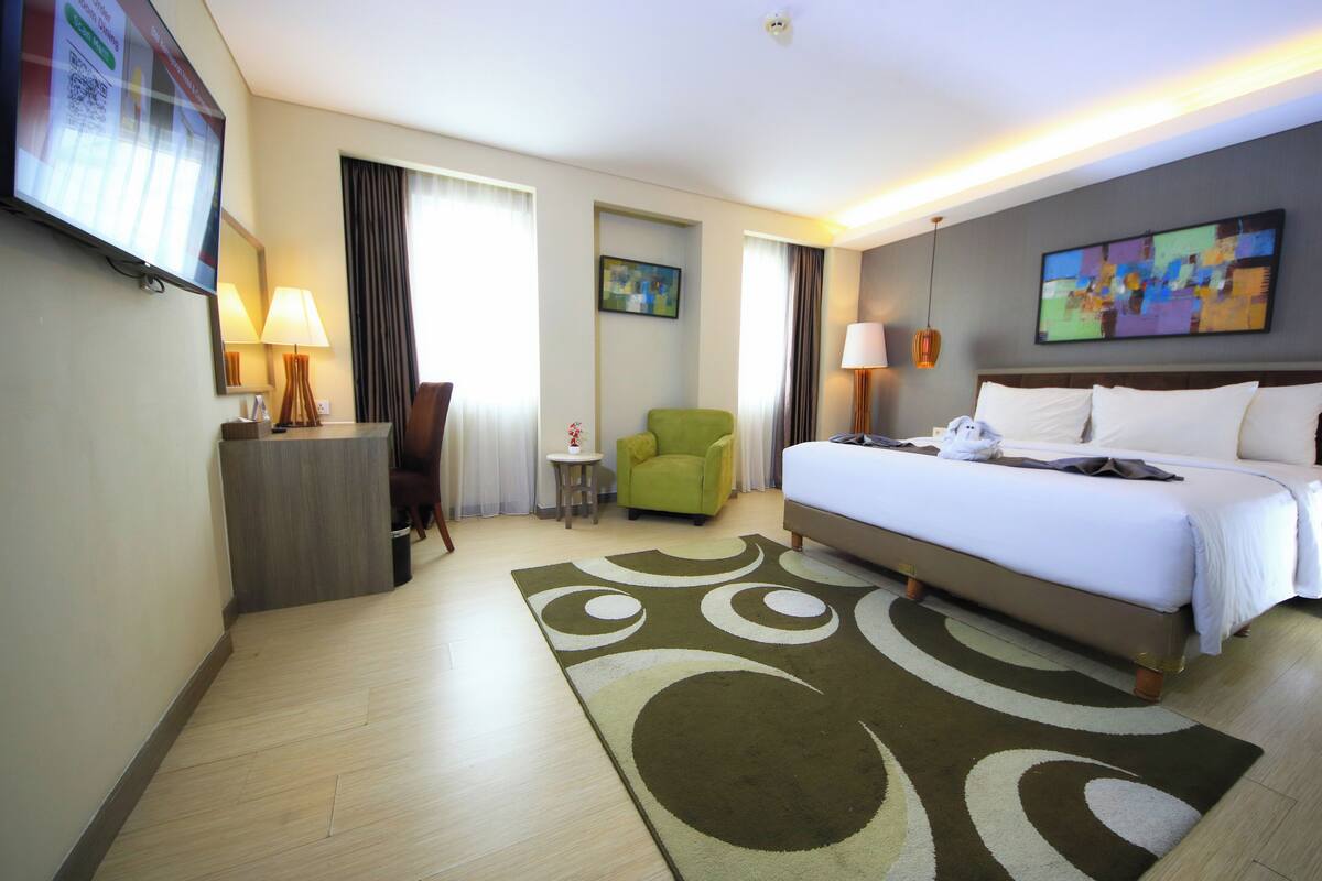A hotel room with a bed, a desk, a chair, a small table, and a television.