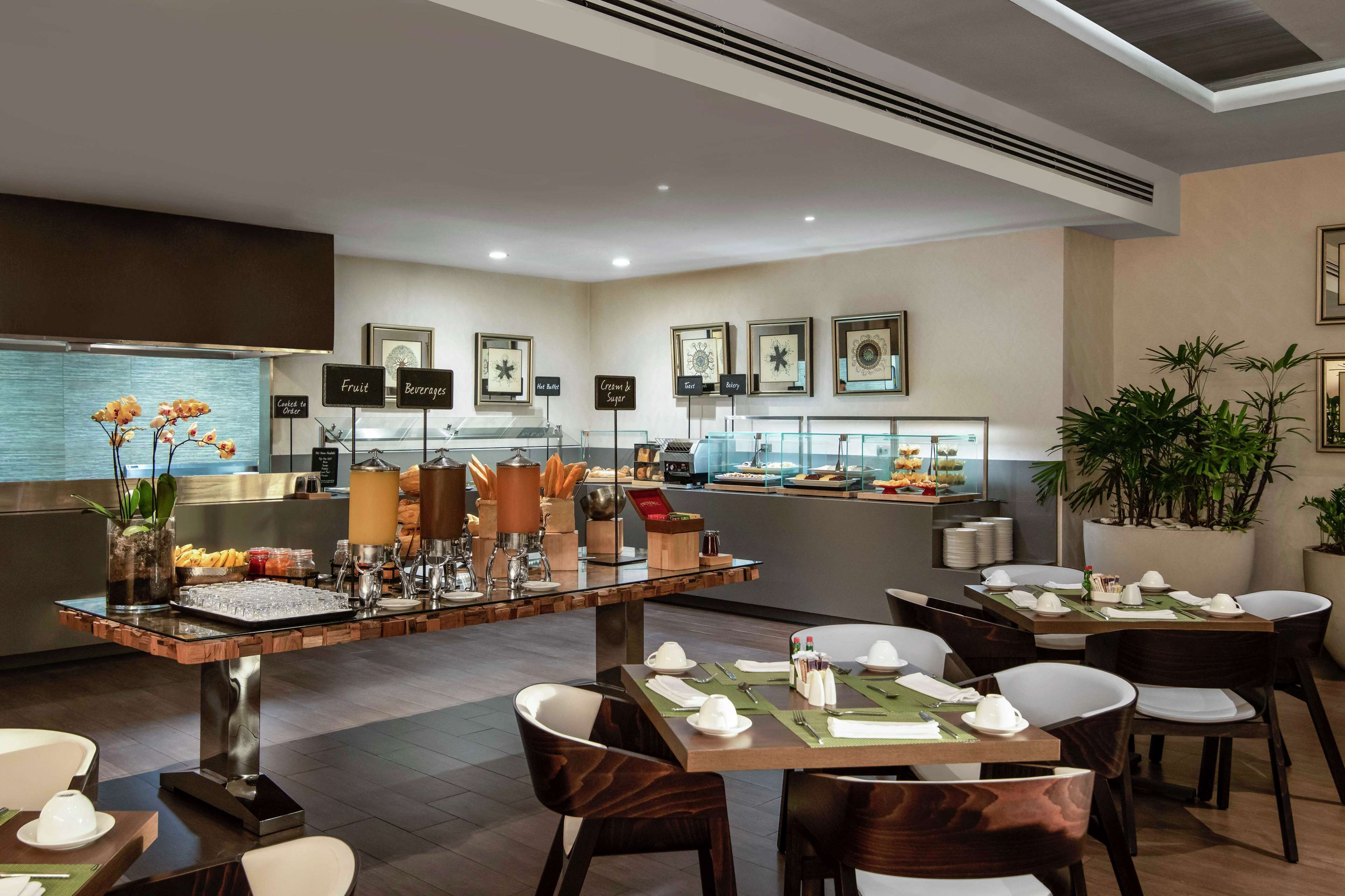 Een modern restaurant met een bar in het midden, meerdere eettafels en een ruim aanbod aan eten en drinken.