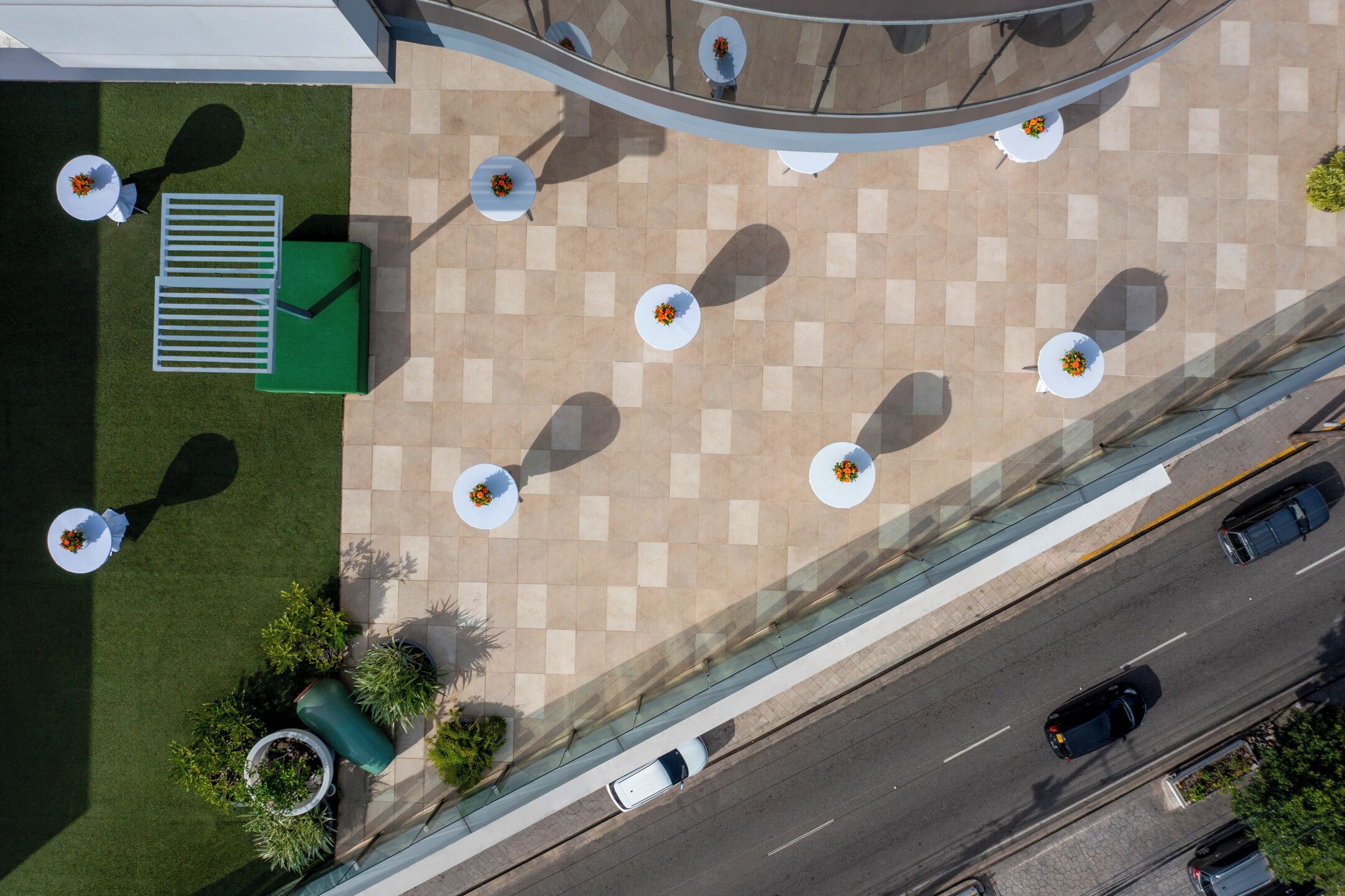 Luchtbeeld van een hotel binnenplaats met terras, een groene zitplaats en een weg met auto's.