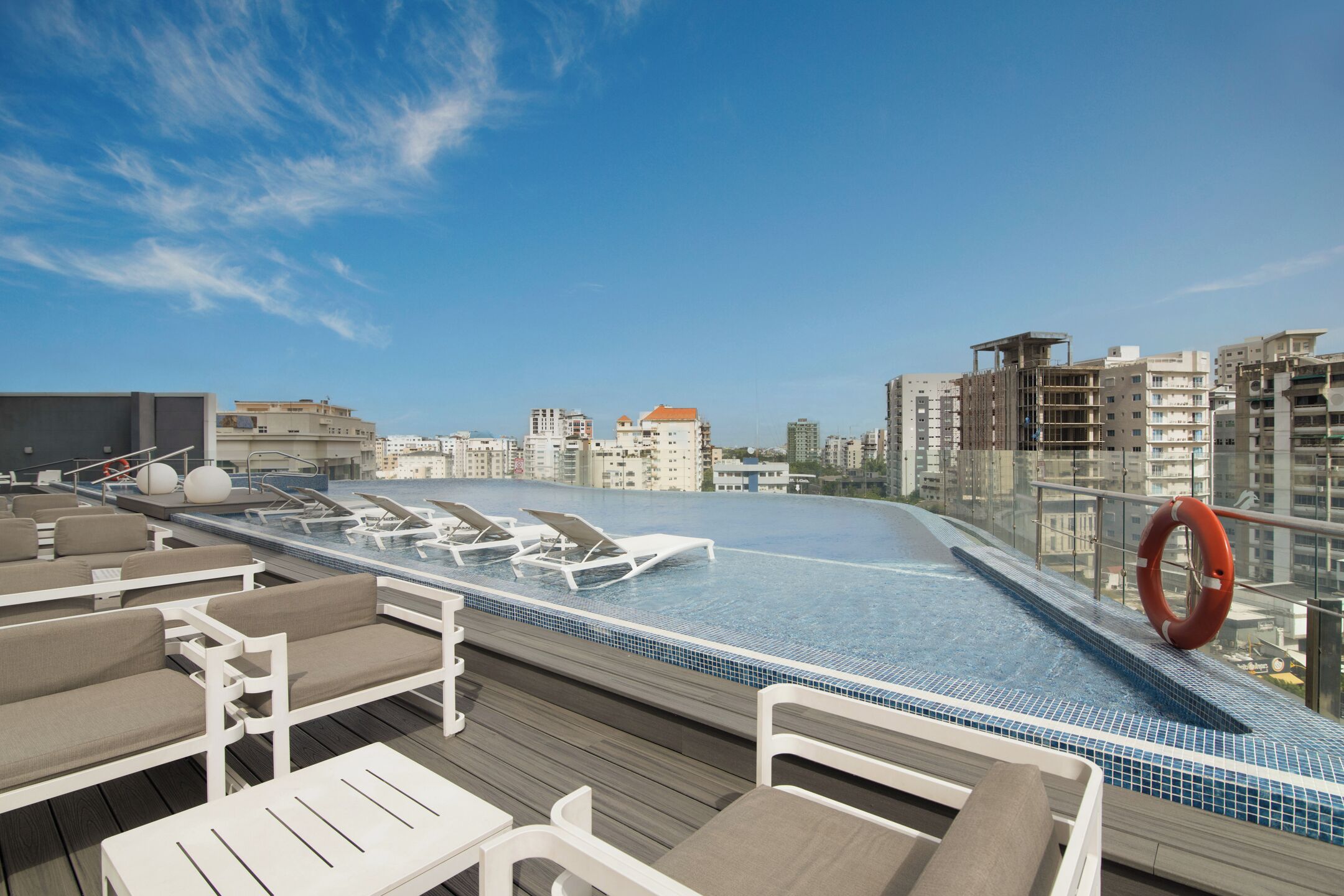A rooftop pool with lounge chairs, a lifebuoy, and a city view.