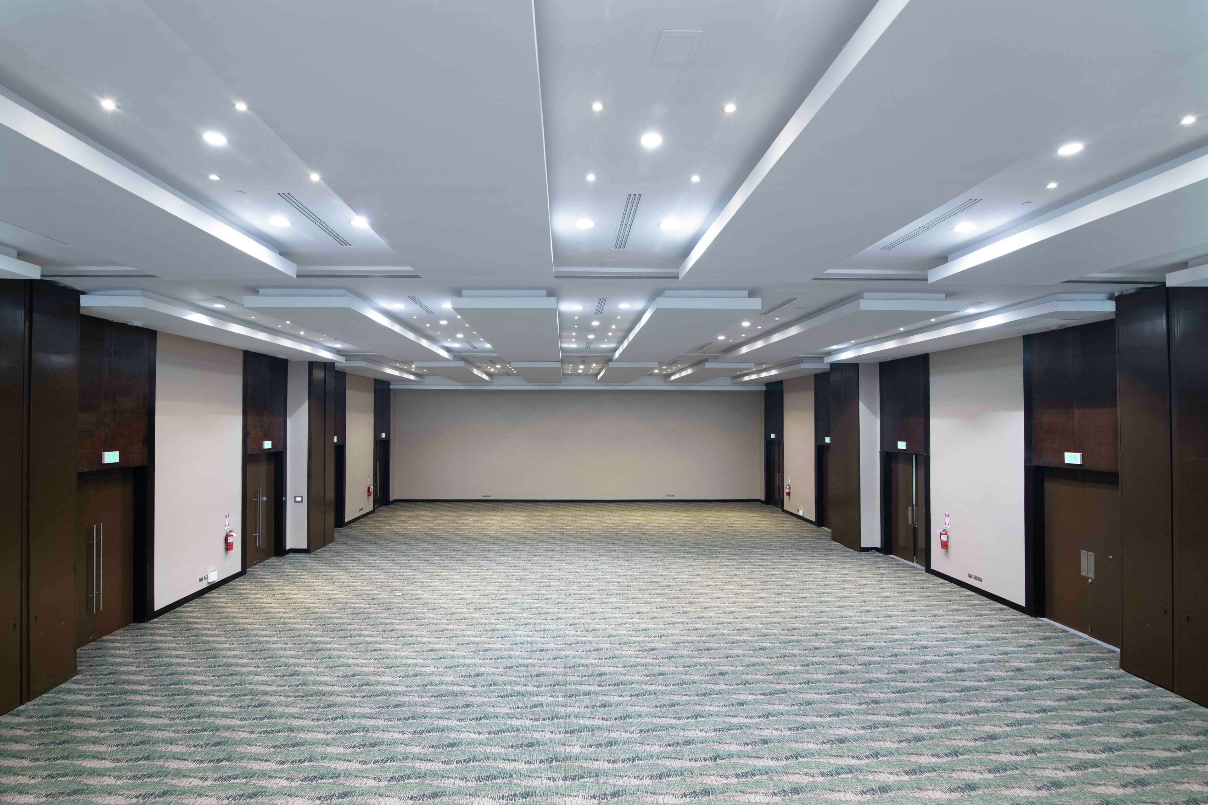 A large, empty conference room with a patterned carpet, recessed lighting, and dark wooden paneling on the walls.