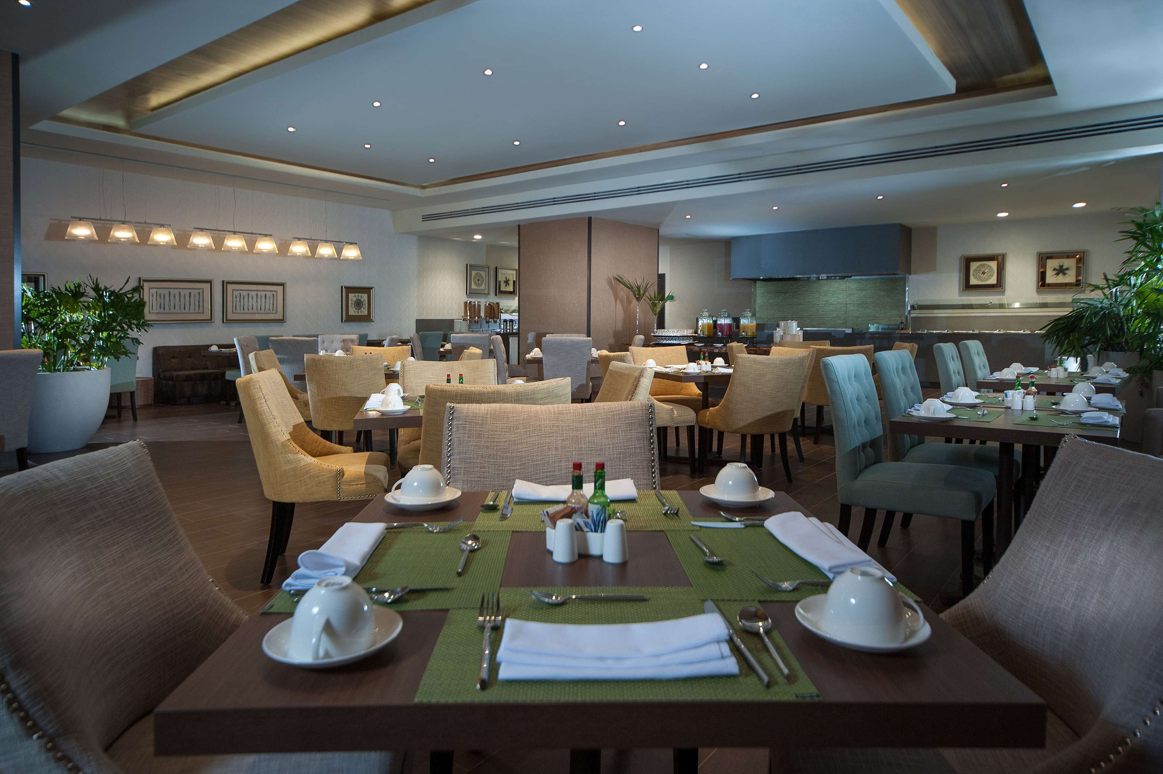 A hotel dining area with multiple tables set for dining, chairs, and a kitchen in the background.