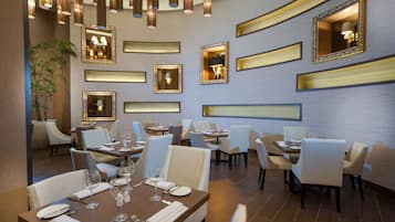 A modern dining area with multiple tables and chairs, decorative mirrors, and pendant lighting.