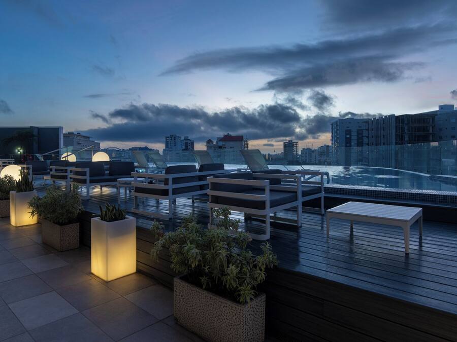 A rooftop terrace with seating, potted plants, and a view of the city skyline.