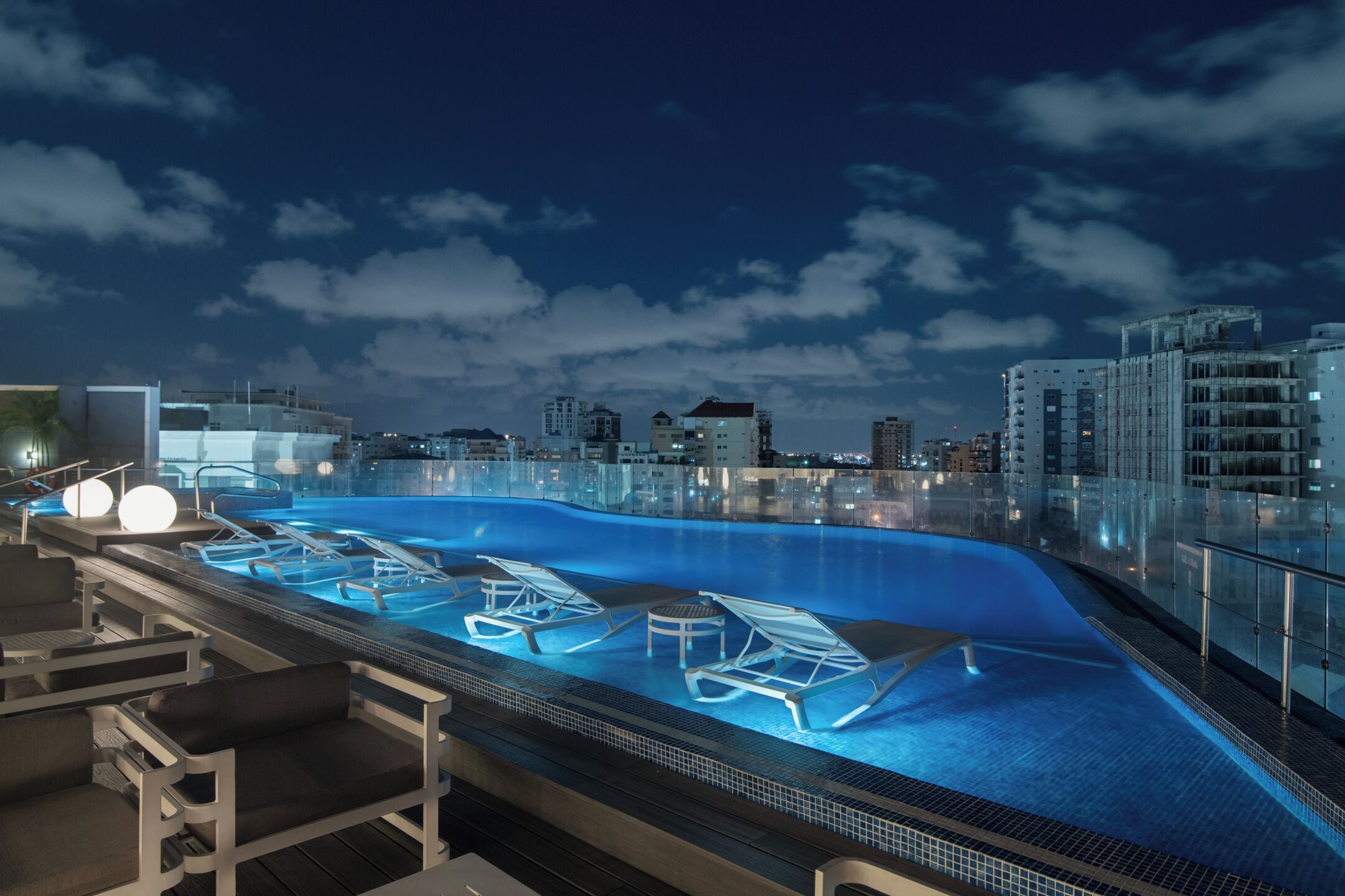 A rooftop infinity pool with lounge chairs and a city skyline in the background.