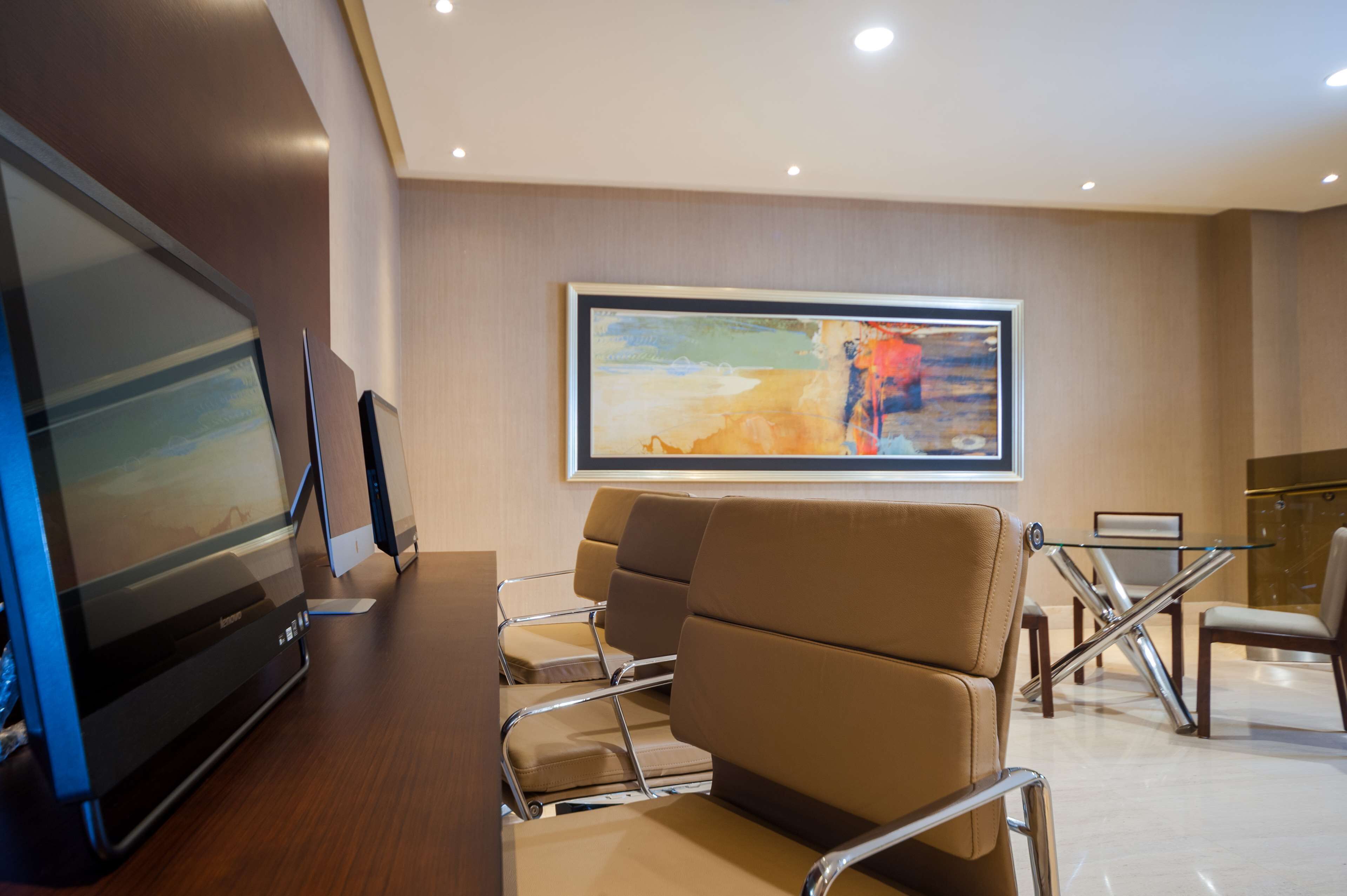 A modern hotel lobby with a large flat-screen TV, comfortable seating, a glass table, and a large abstract painting on the wall.