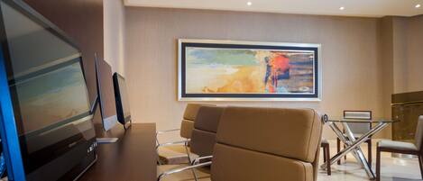 A modern hotel lobby with a large flat-screen TV, comfortable seating, a glass table, and a large abstract painting on the wall.