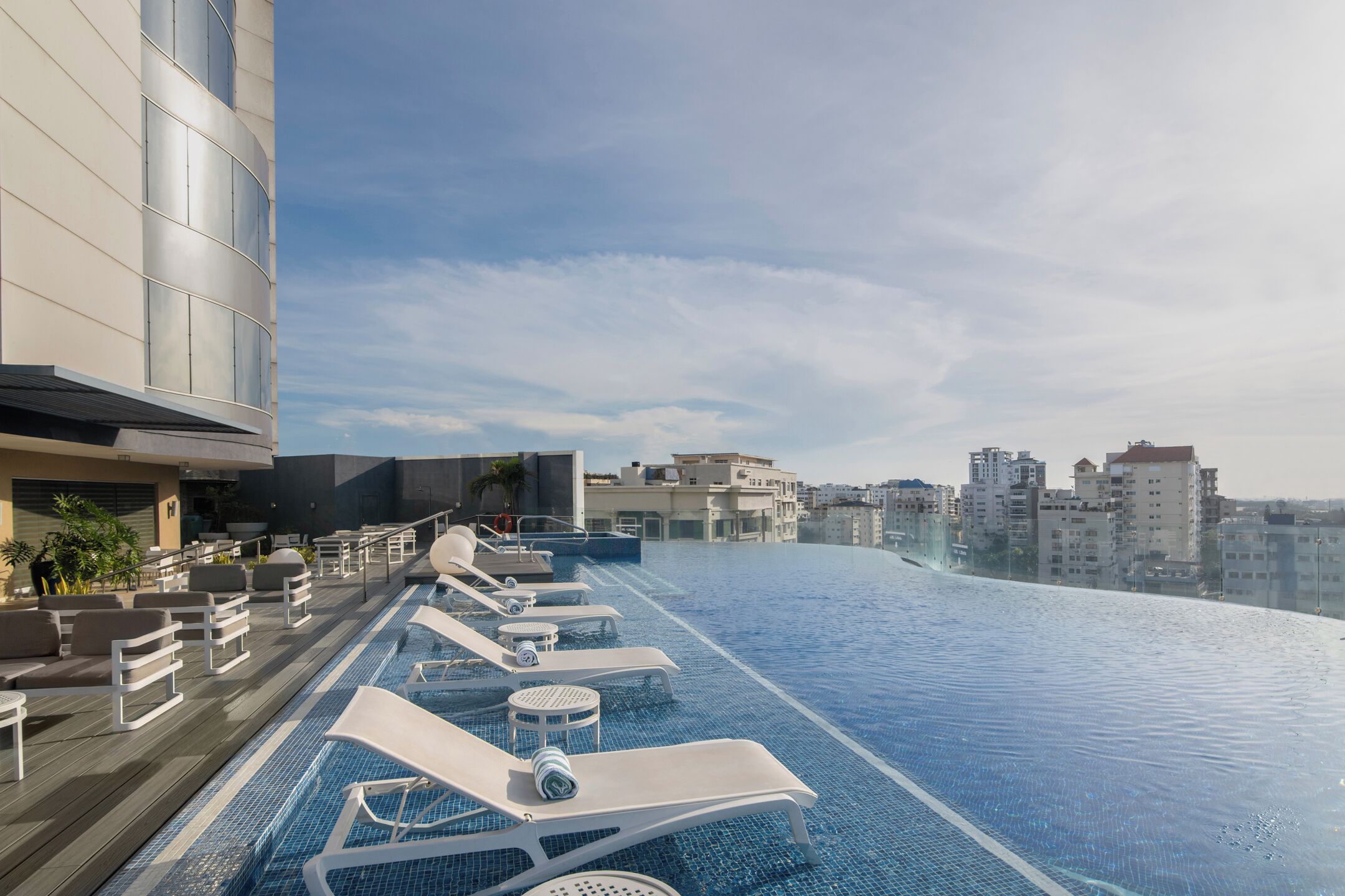 Una piscina a sfioro sul tetto con lettini e un edificio moderno sullo sfondo.