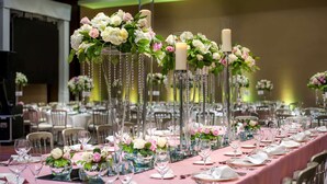 Une salle de banquet avec de longues tables dressées pour un événement formel, décorée de compositions florales et de chandeliers.