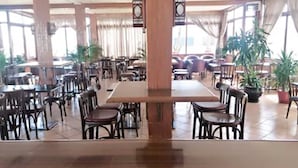 Un amplio comedor interior con varias mesas y sillas, ventanas grandes y plantas en macetas.