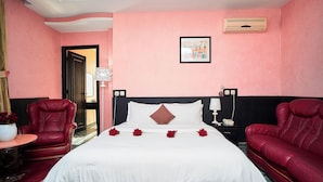 Habitación de hotel con cama, dos sillones de cuero rojo, una mesita de noche con lámpara y aire acondicionado de pared.