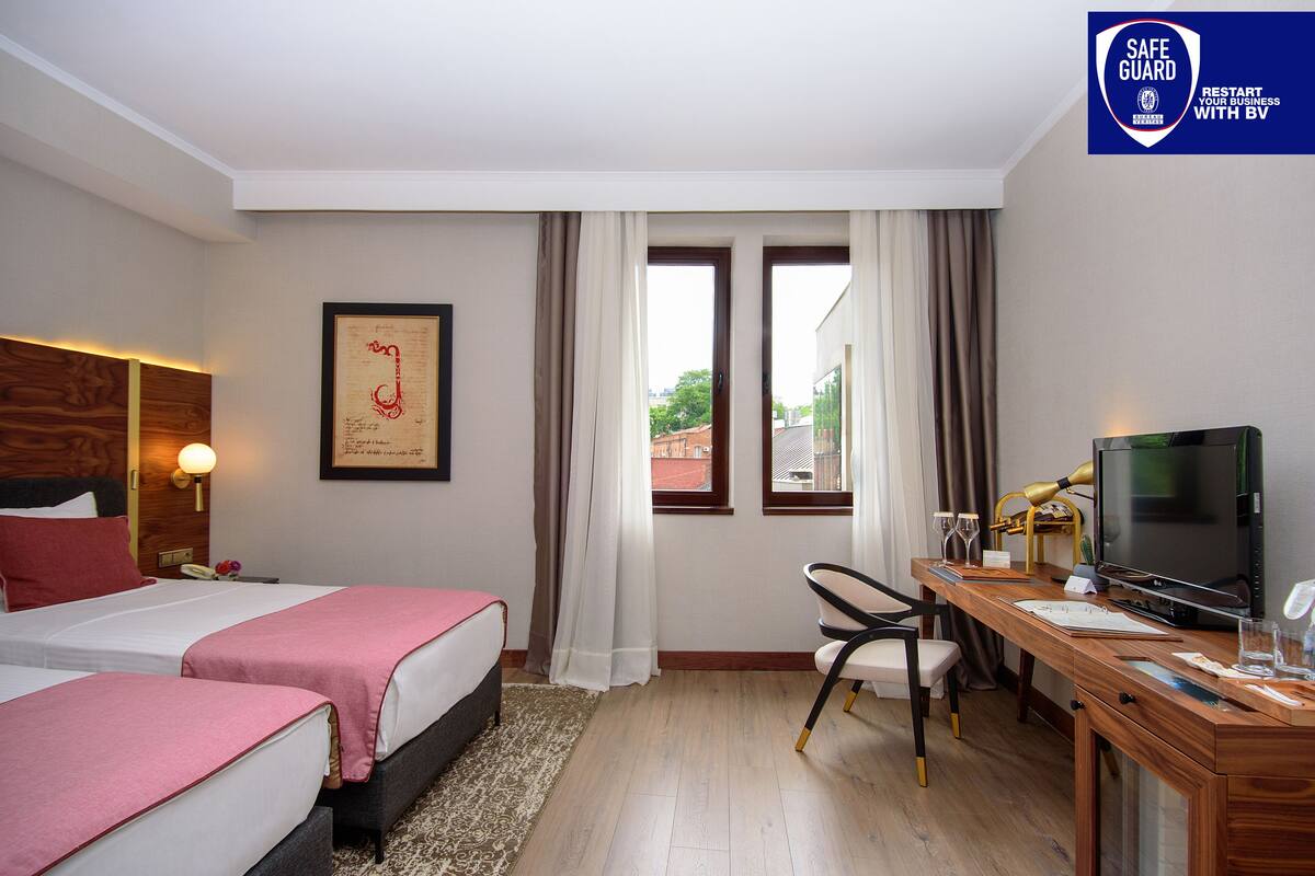 A hotel room with two beds, a desk with a computer, a TV, and a view of the outside.