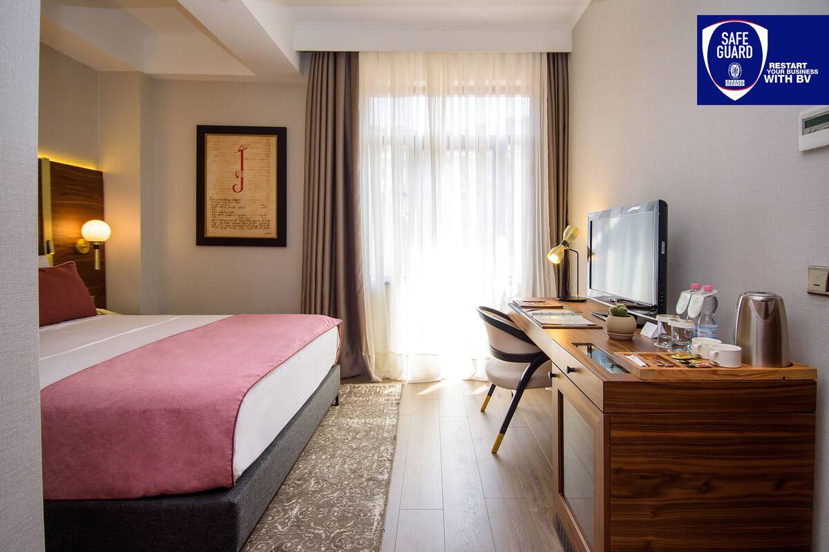 A hotel room with a bed, desk, chair, television, and a safe guard sign.