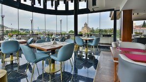 Ein Restaurant mit modernem Interieur, blaue Stühle, Holztische und im Hintergrund ein Blick auf ein historisches Gebäude.