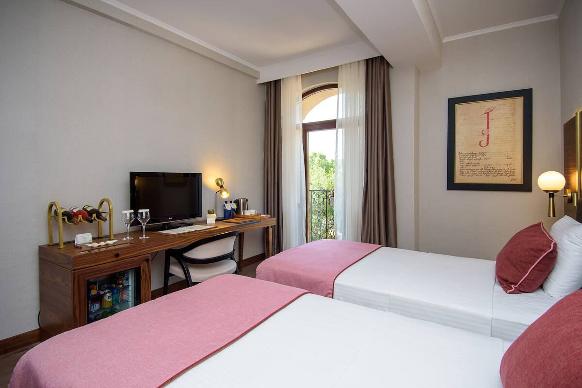 A hotel room with two beds, a desk with a computer, a TV, and a window with curtains.