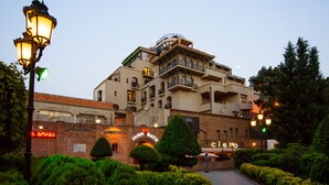 Ein mehrstöckiges Hotel mit markanter Eingangsfassade, einem gepflegten Garten und blauem Himmel.