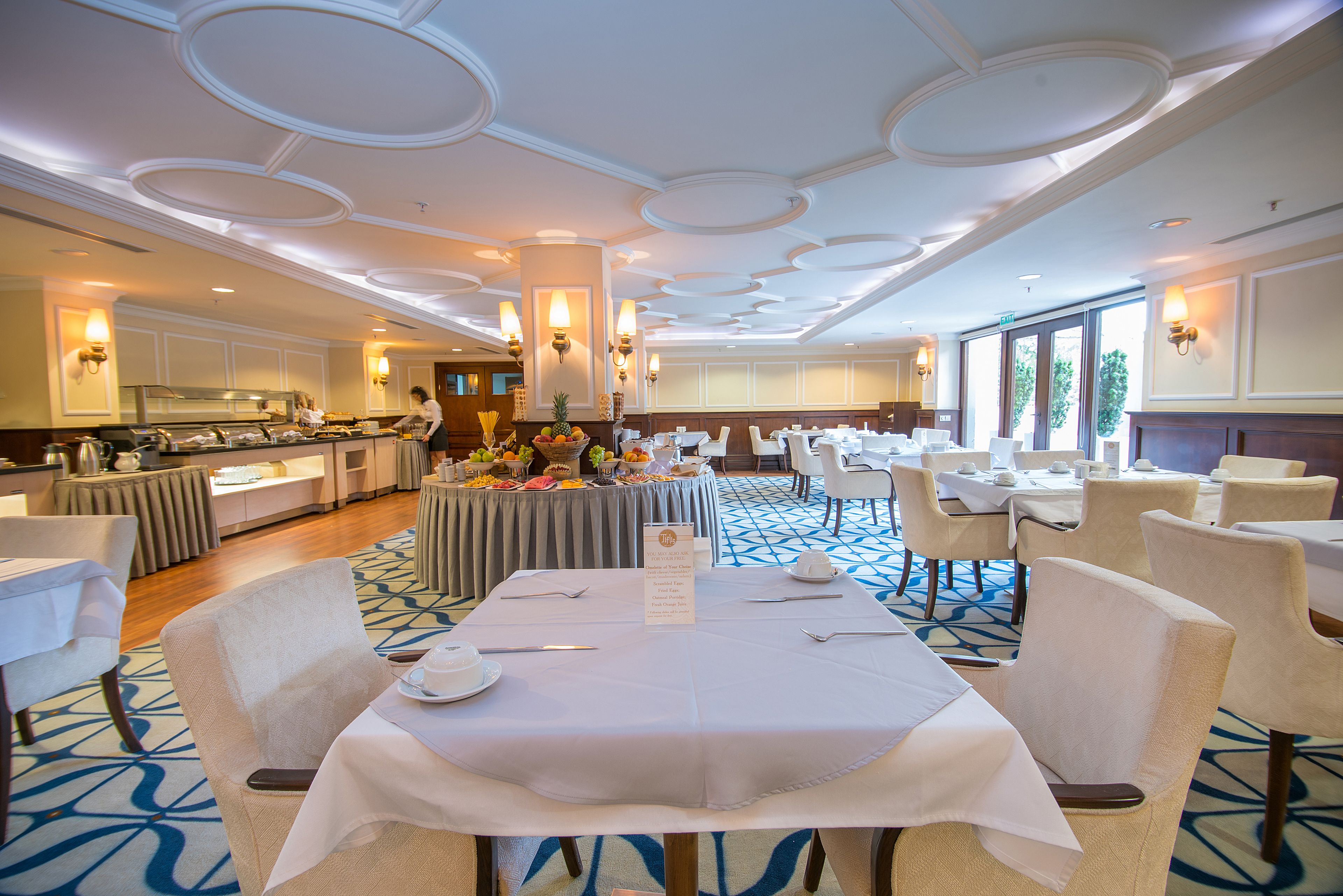 Un comedor de hotel con mesas redondas, sillas y un bufé.
