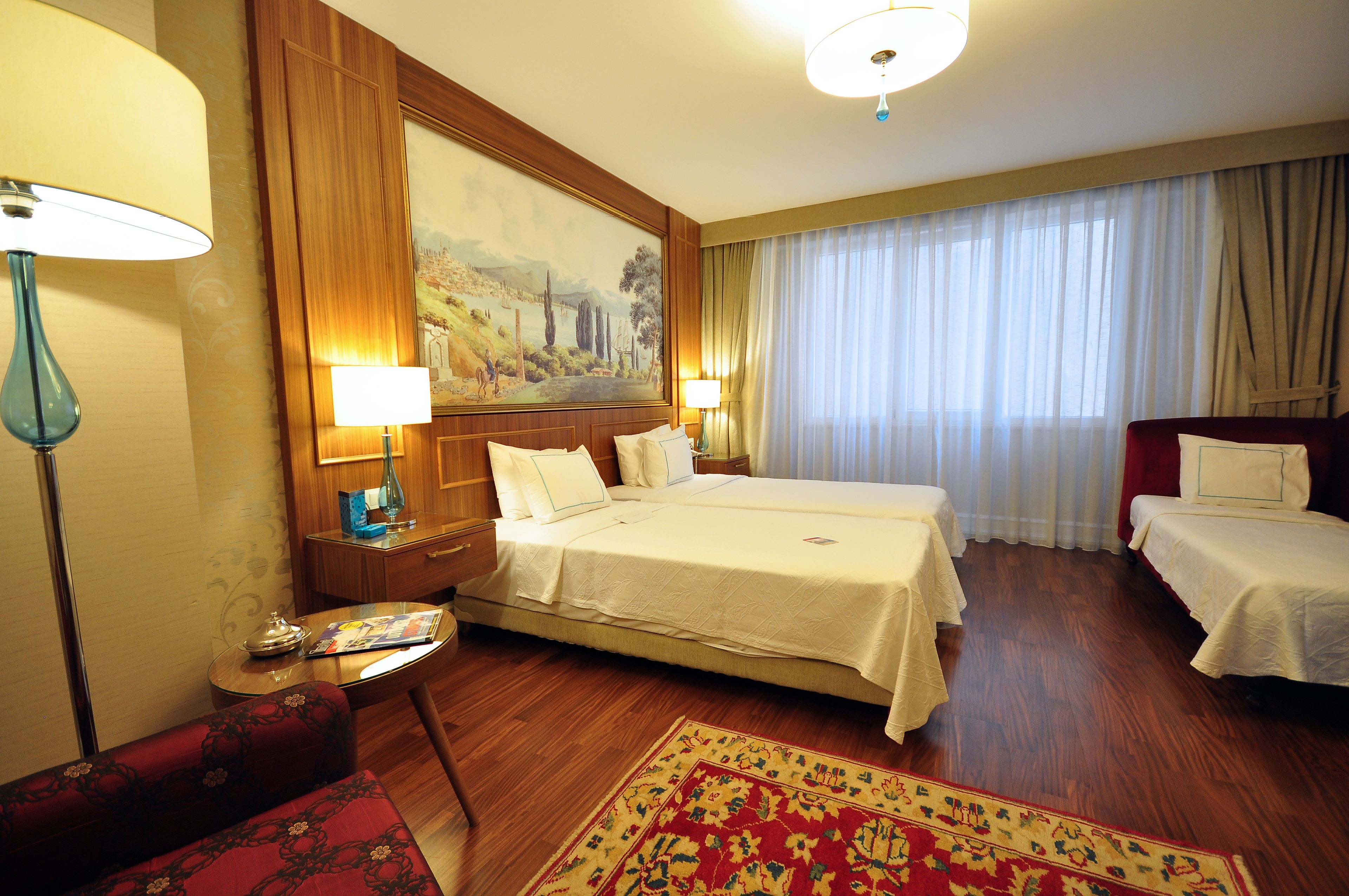 A hotel room with a large bed, two bedside tables, a desk, a chair, and a large painting on the wall.