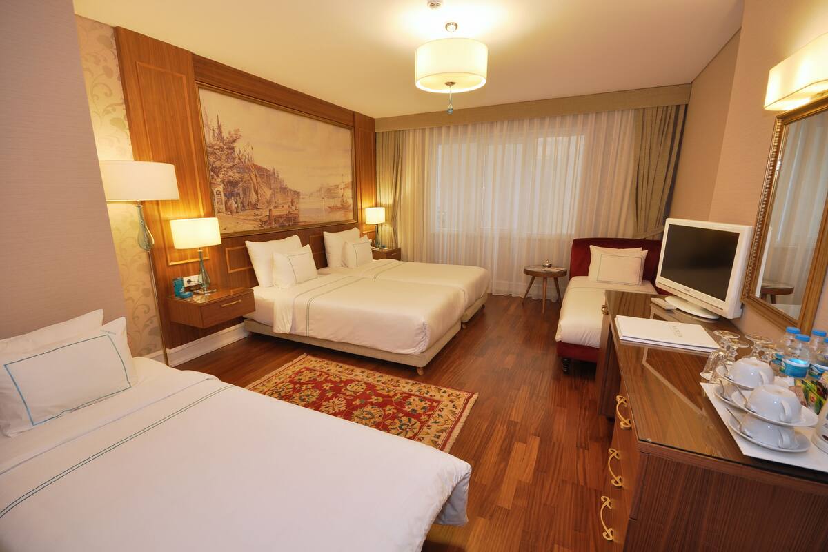 A hotel room with two beds, a desk with a computer, a chair, and a large painting on the wall.