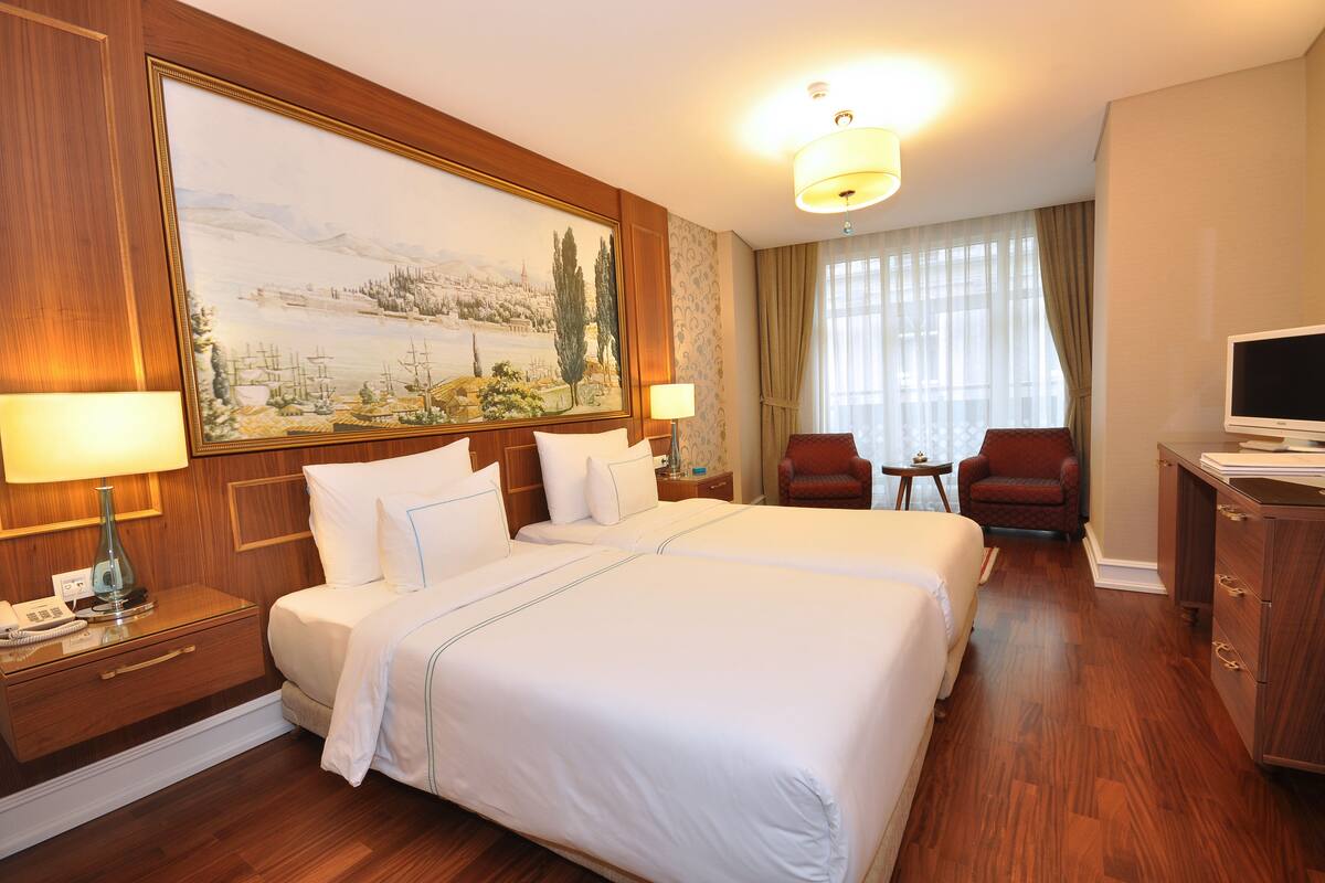 A hotel room with a large bed, two bedside tables, a TV, a desk, and a chair.