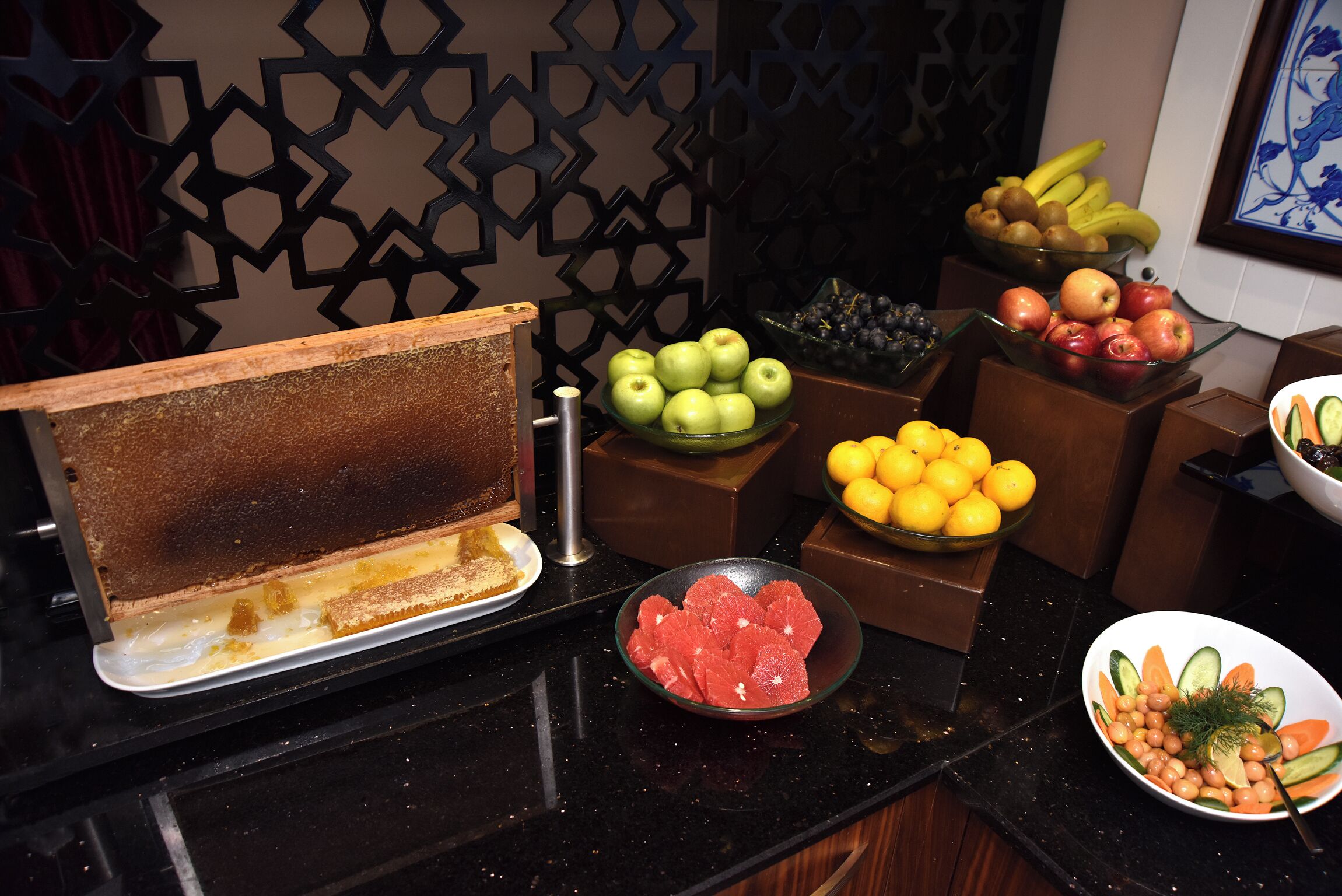 A buffet table with various fruits and vegetables, including apples, oranges, and cucumbers.