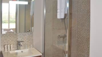 Un baño con ducha de vidrio, un lavabo con espejo y una toalla colgada en la puerta de la ducha.