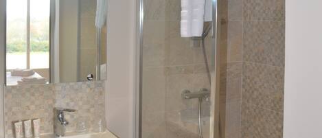 Un baño con ducha de vidrio, un lavabo con espejo y una toalla colgada en la puerta de la ducha.