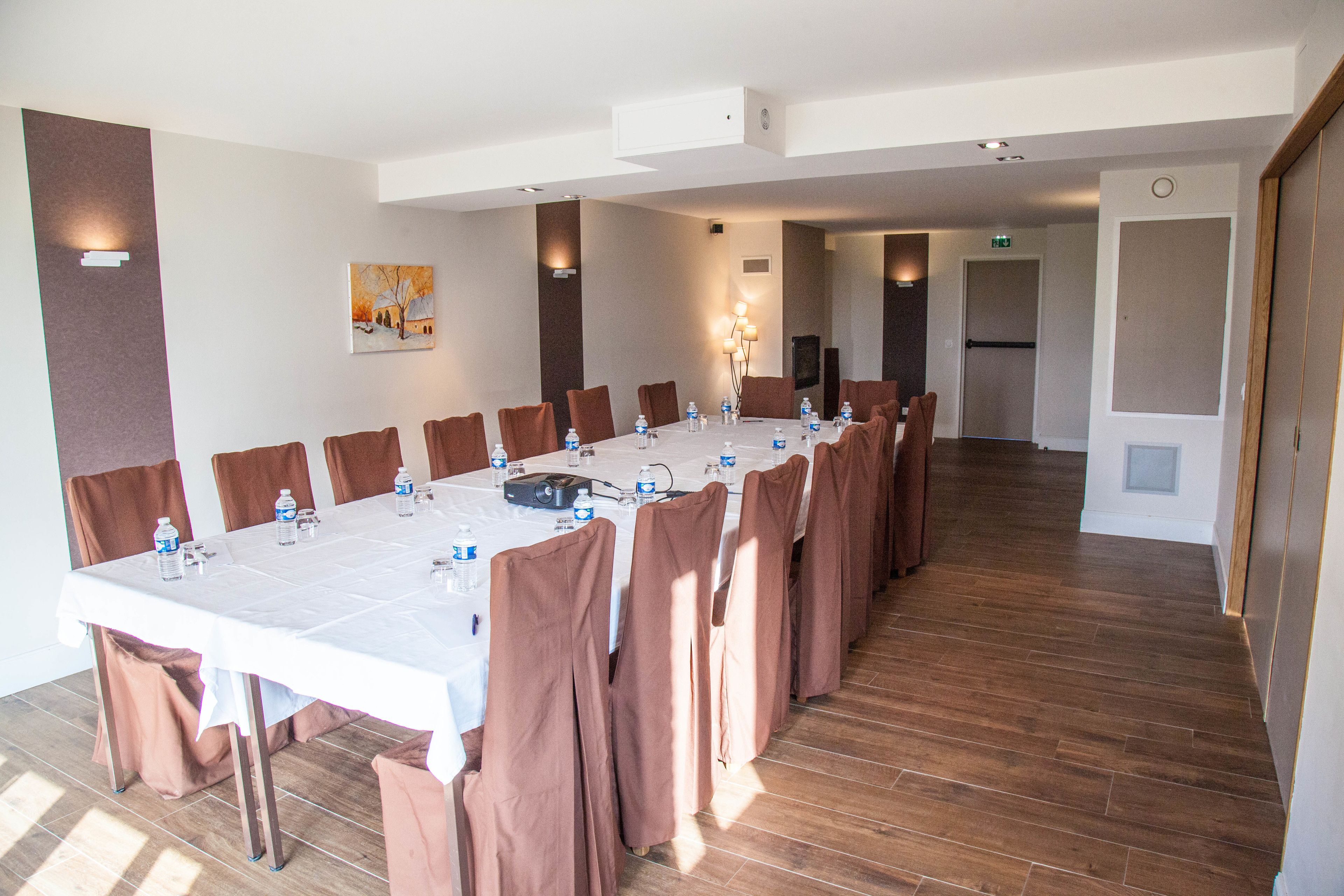 Un salón de conferencias con una larga mesa, sillas marrones y botellas de agua.