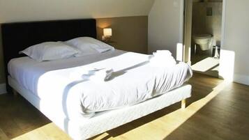 A neatly made bed with white linens in a room with wooden flooring and a dark headboard.